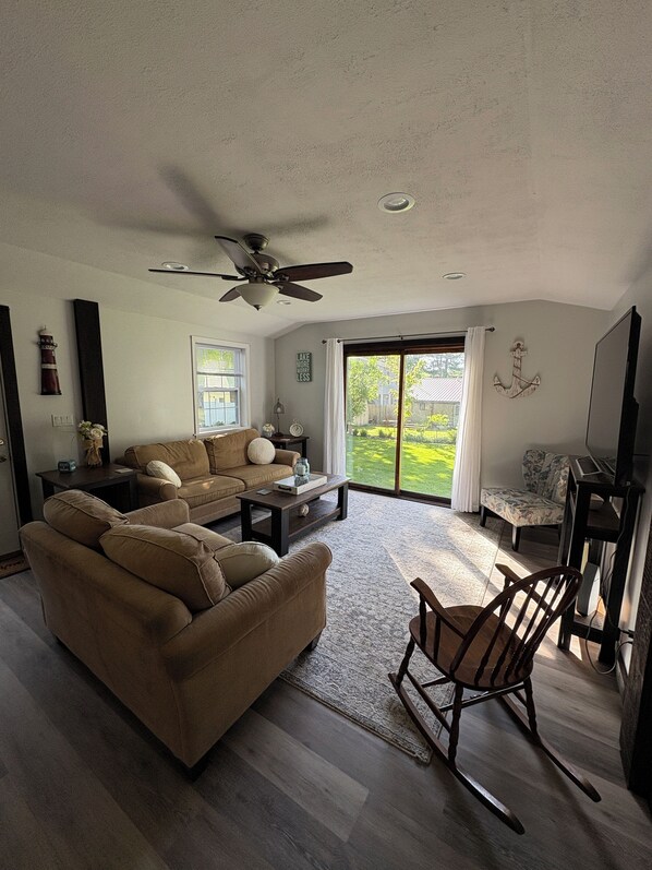 A spacious living room with a large brown sectional sofa, a wooden rocking chair, and a ceiling fan.