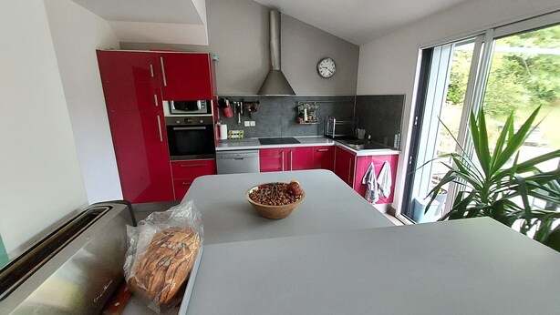 A modern kitchen with red cabinets, a white countertop, a toaster, a bread loaf, and a bowl of nuts.