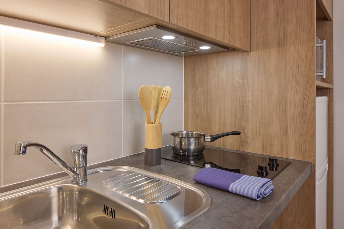 A modern kitchen with a stainless steel sink, a stove, wooden cabinets, and a pot.