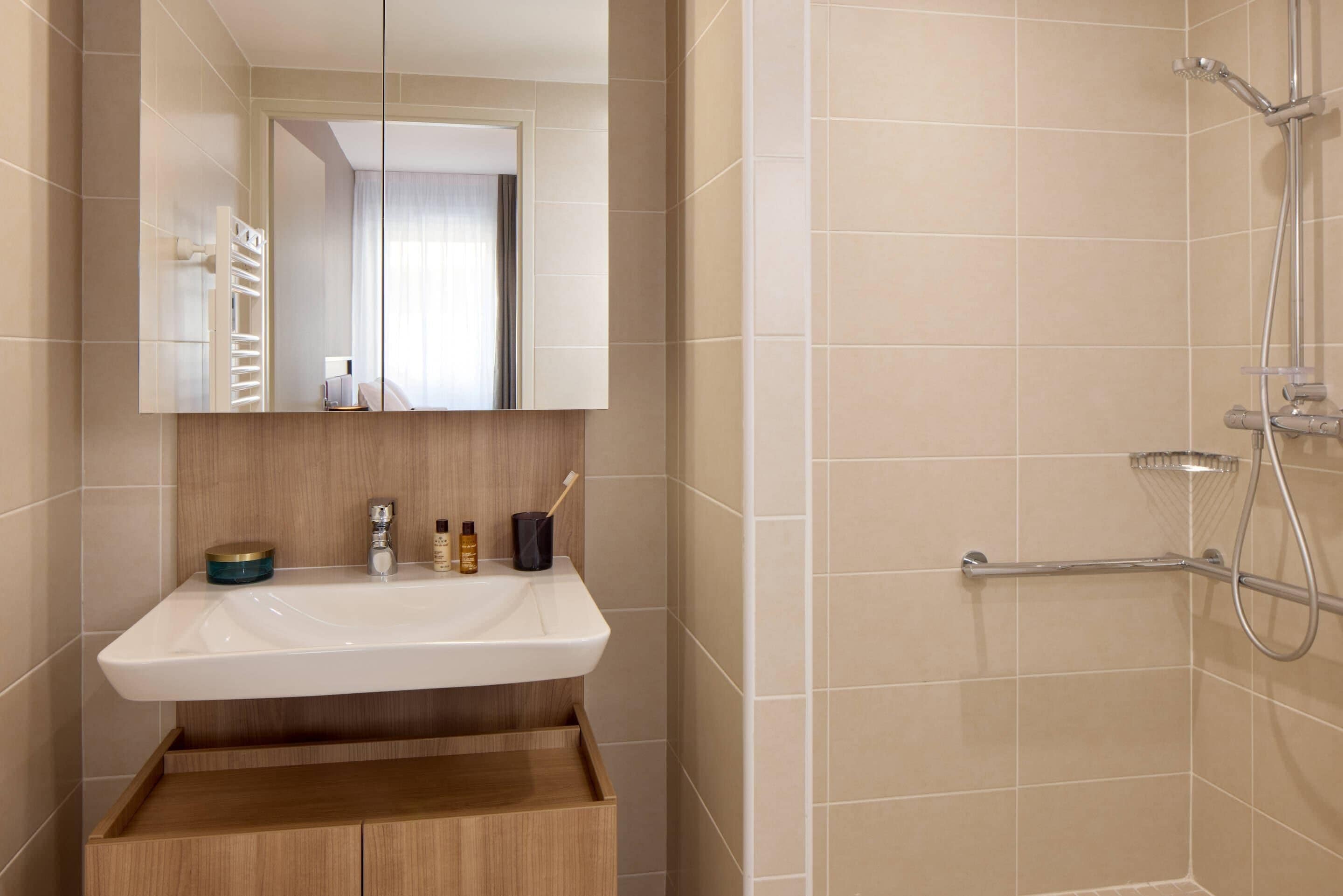 A bathroom with a white sink, a mirror, a wooden cabinet, and a shower area.