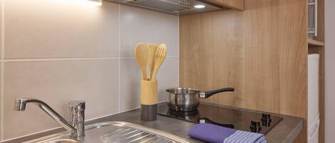 Cocina moderna con pileta de acero inoxidable, estufa, alacenas de madera y una olla con espátula.