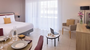 Quarto de hotel com cama, escrivaninha, cadeira, mesa de jantar, pratos e copos, e um laptop.