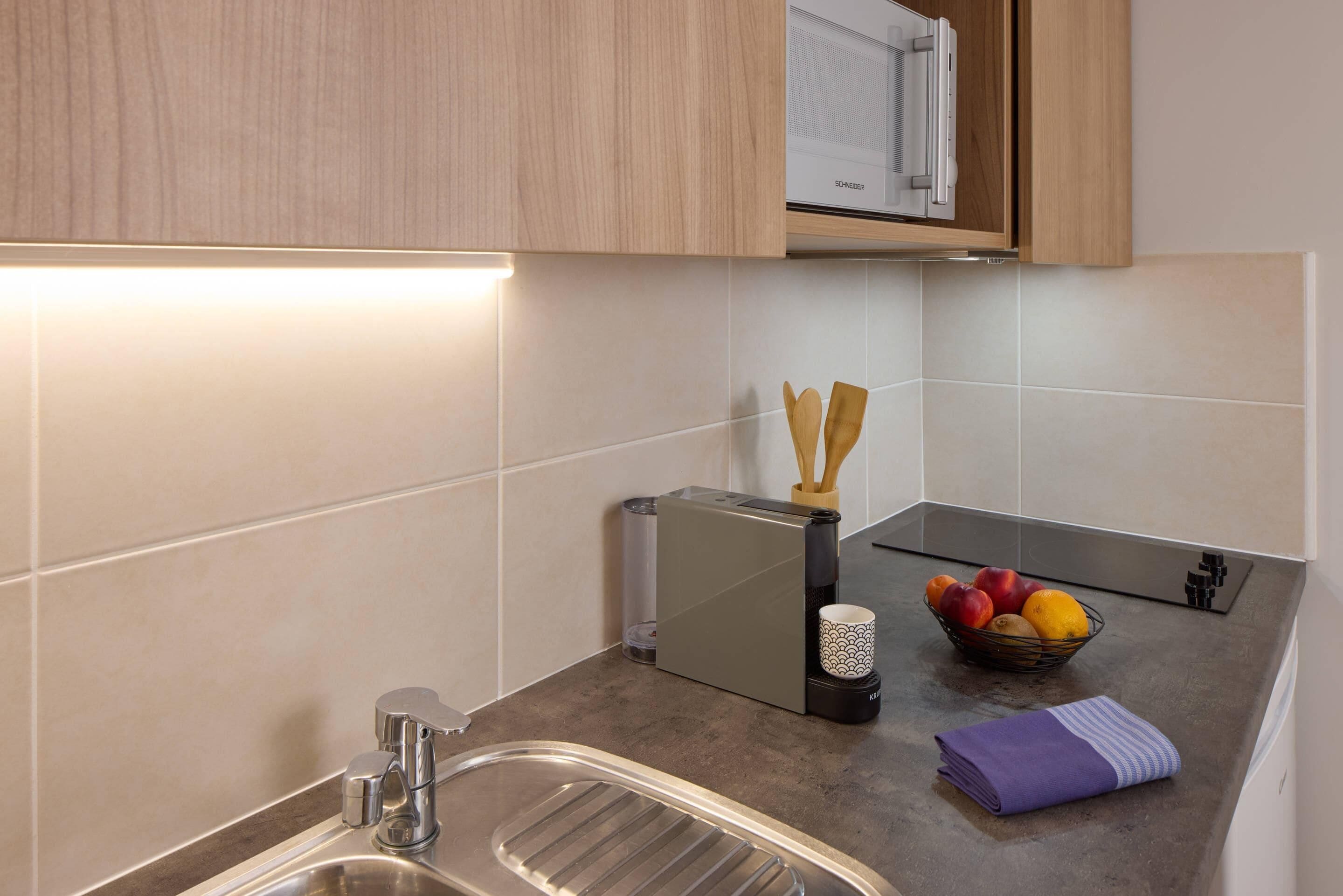 Una cocina moderna con un lavamanos de acero inoxidable, un microondas y un frutero en la encimera.