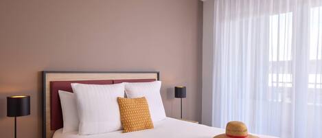 A neatly made bed with white and yellow pillows, a magazine, and a straw hat on the bed.