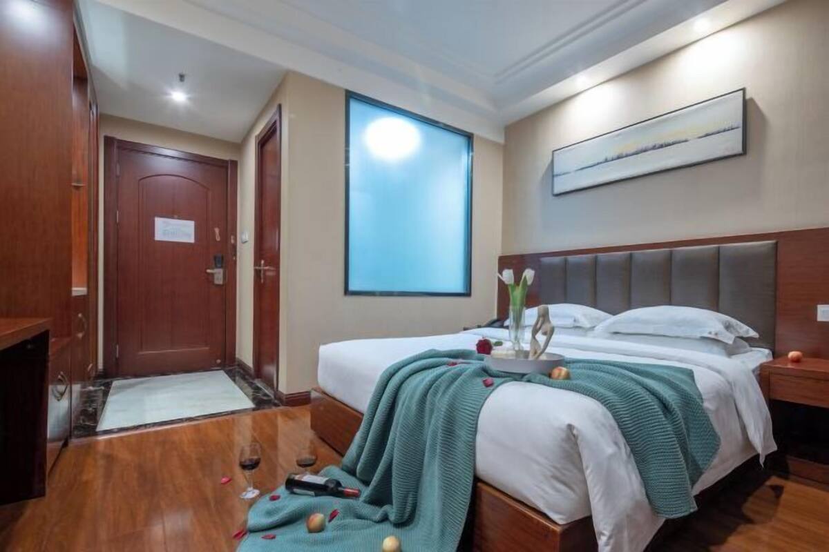 Une chambre d’hôtel avec un lit, une table de chevet, un tableau au mur et une porte.