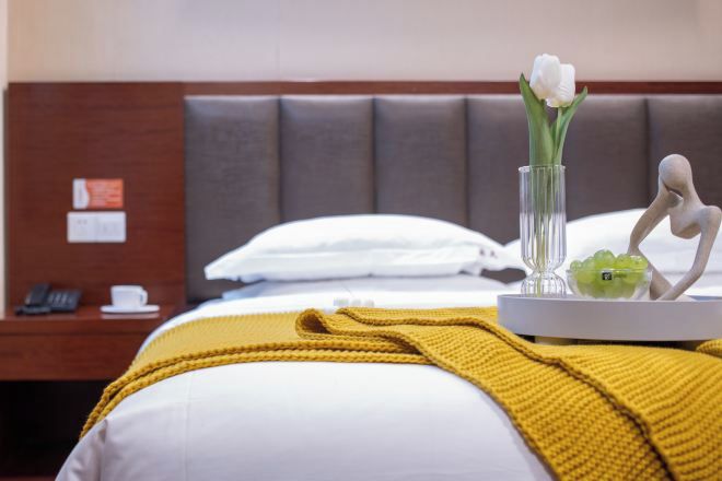 Ein Hotelzimmer mit einem Bett, einem Nachttisch mit Telefon, einer Vase mit Blumen und einem dekorativen Gegenstand auf dem Tisch.
