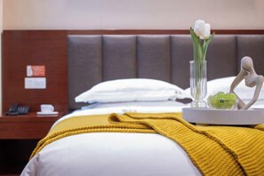A hotel room with a bed, a bedside table with a phone, a vase with flowers, and a decorative item on the table. - Forever Star Hotel (Fuyang)