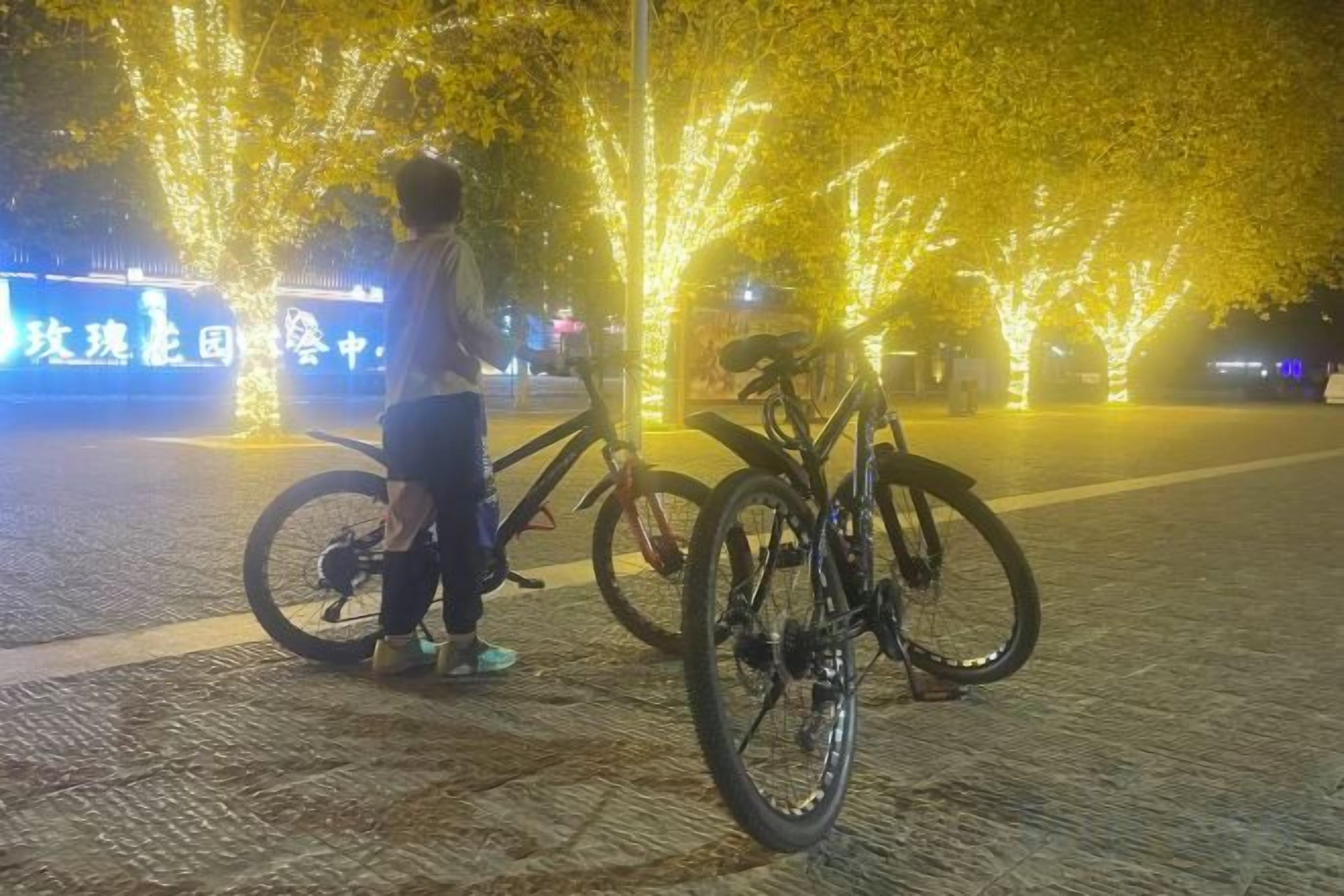 Une personne se tient à côté d’un vélo sur une surface pavée, avec des arbres en arrière-plan.
