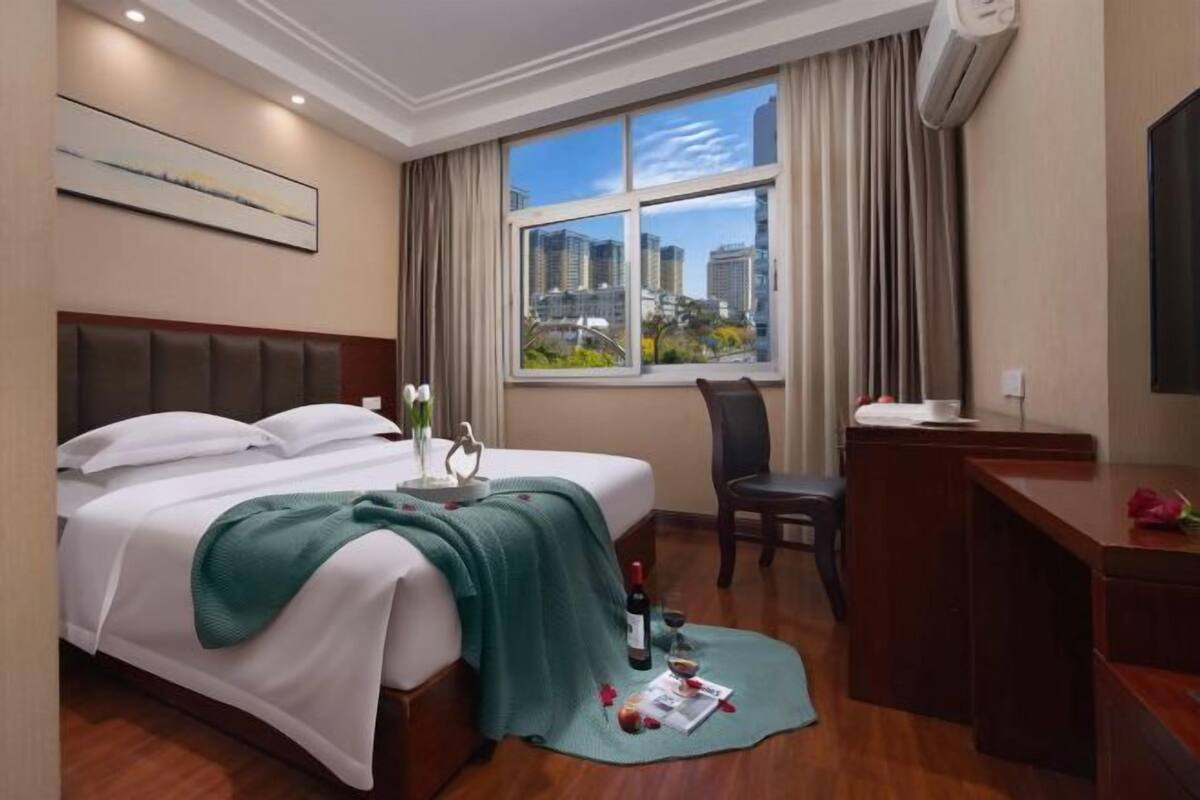 Une chambre d’hôtel équipée d’un lit, d  ’un bureau, d’une chaise, d’une fenêtre donnant sur la ville et d’un appareil de climatisation.