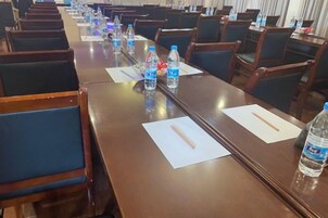Un salón de conferencias con mesas largas, sillas y botellas de agua.