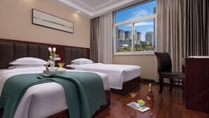 Une chambre d’hôtel avec deux lits, une grande fenêtre donnant sur la ville, un bureau et une chaise.