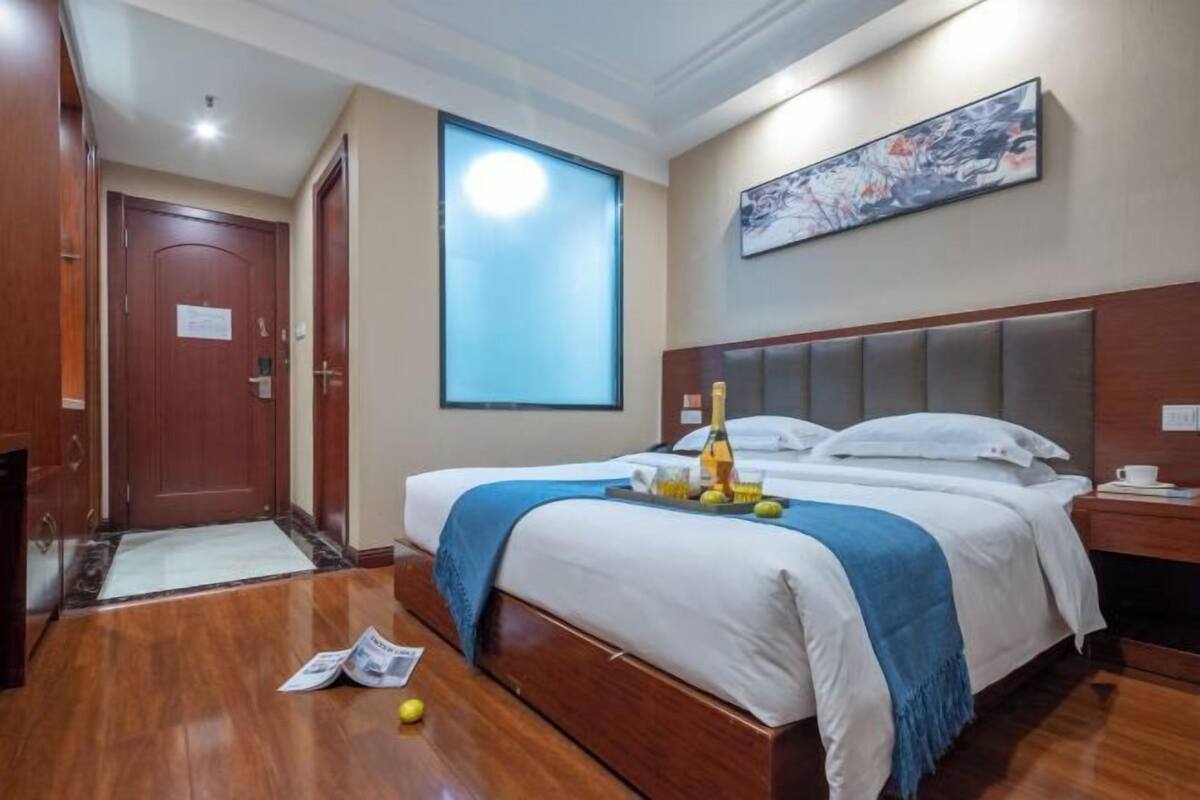 Une chambre d’hôtel avec un grand lit, une table de chevet, une fenêtre avec des stores, une porte et un tableau au mur.