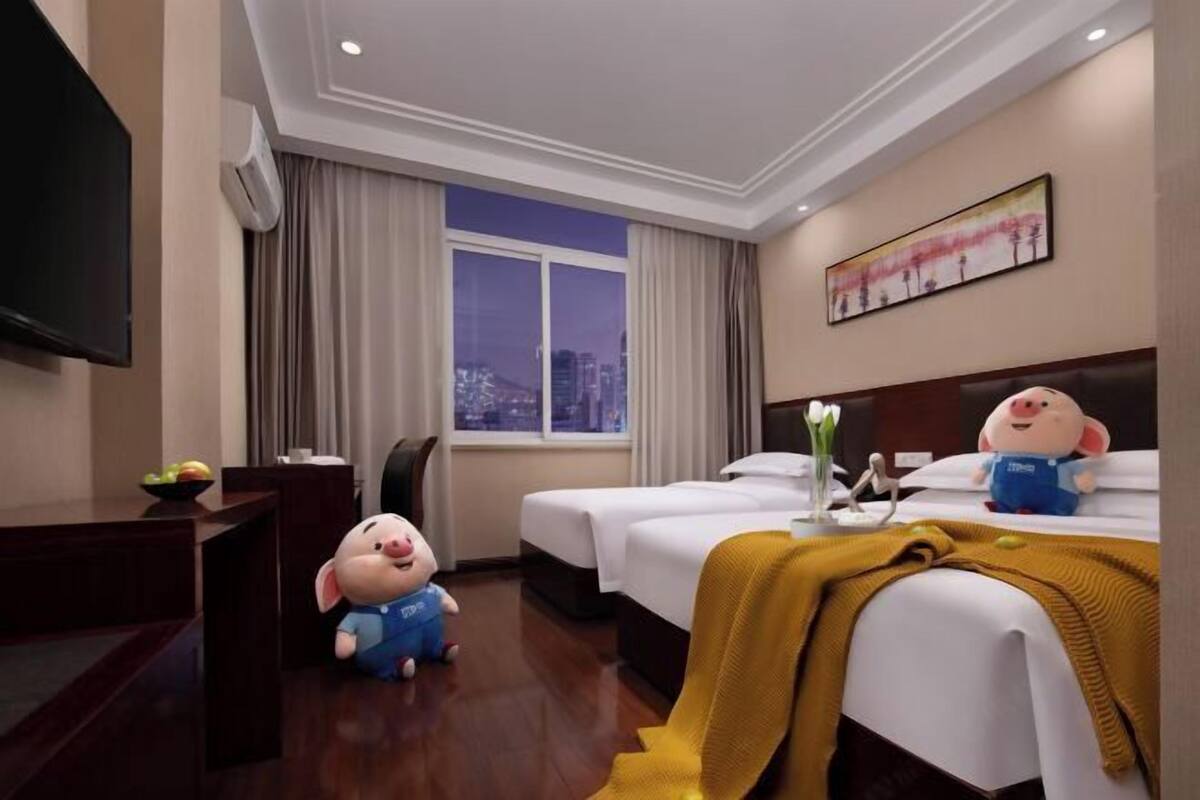 Une chambre d’hôtel avec deux lits, une télévision, un bureau avec un panier de fruits et une fenêtre donnant sur la ville.