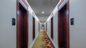 Un couloir d’hôtel avec des portes en bois, des panneaux indiquant le numéro des chambres et un sol recouvert de moquette.