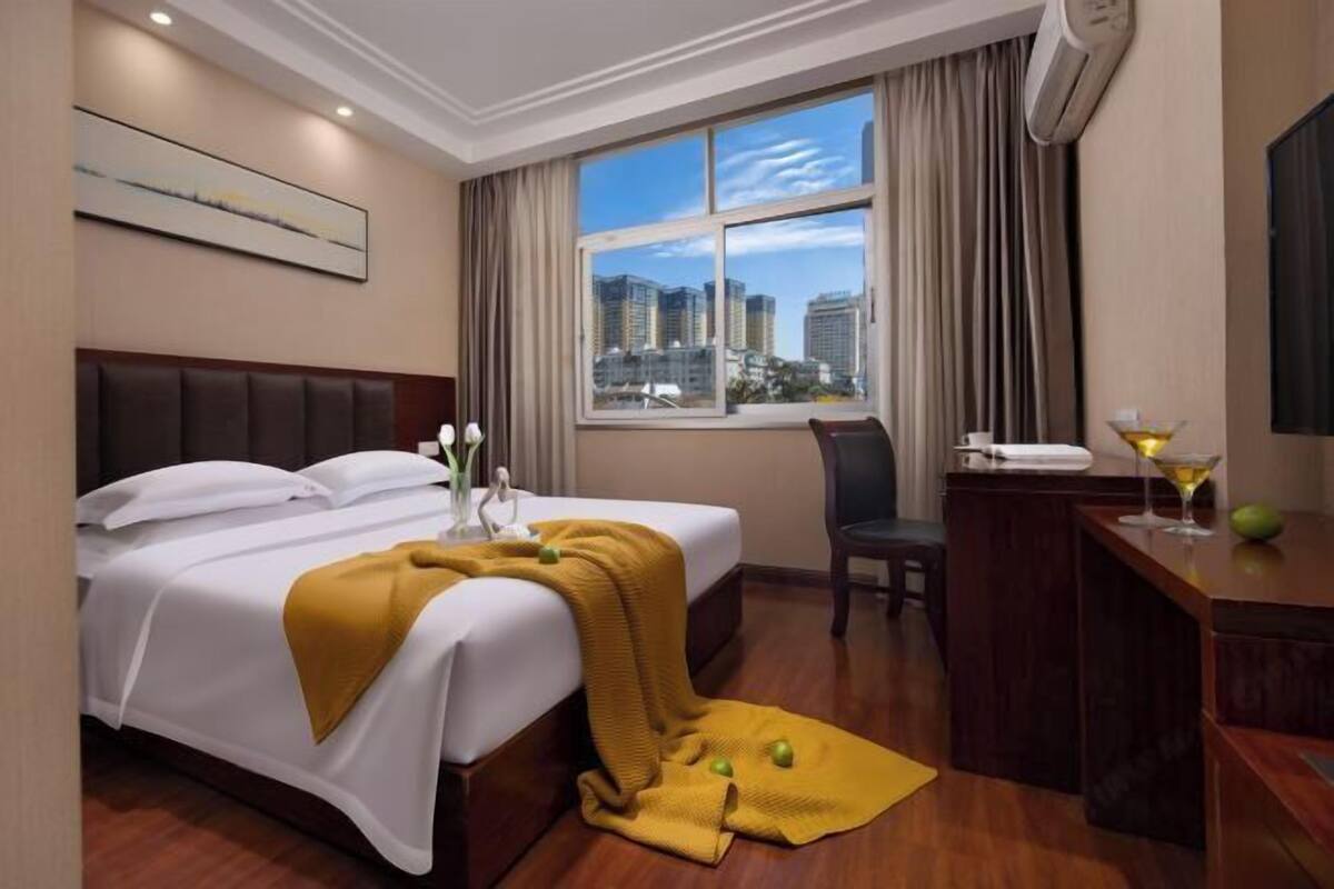 Une chambre d’hôtel équipée d’un lit, d’un bureau, d’une chaise, d’une fenêtre donnant sur la ville et d’un appareil de climatisation.