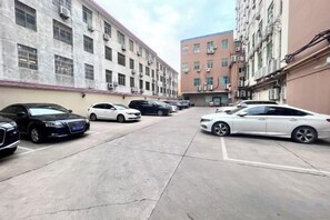 Un parking où sont garées plusieurs voitures devant un immeuble à la façade en briques rouges.