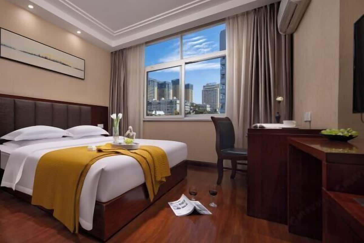 Une chambre d’hôtel équipée d’un lit, d’un bureau, d’une chaise, d’une fenêtre donnant sur la ville et d’un appareil de climatisation.