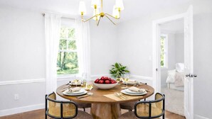 A dining room with a round wooden table, four chairs, a chandelier, and a bowl of fruit.