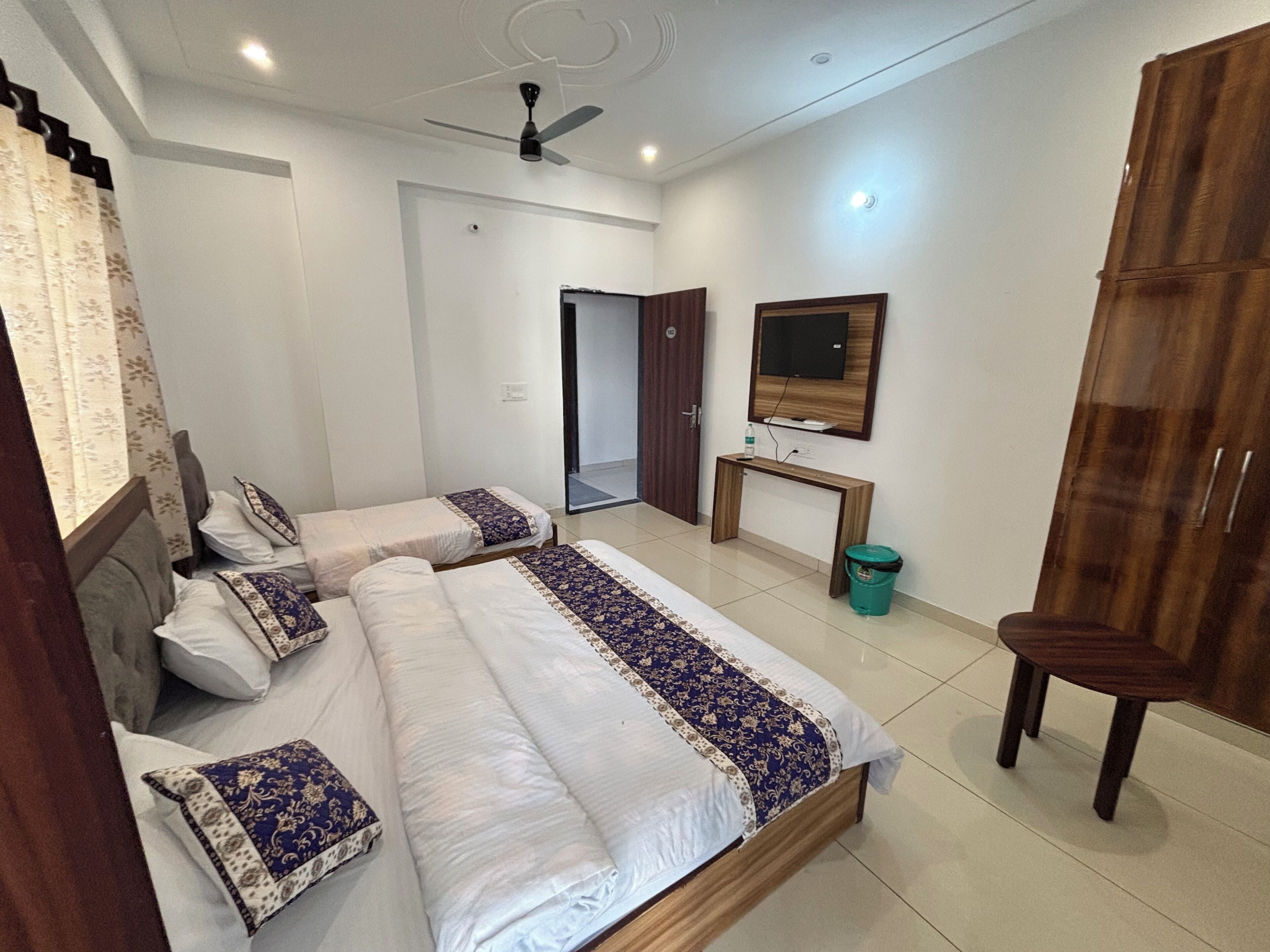 A bedroom with two beds, a desk, a chair, a television, and a wardrobe.