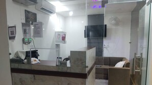 A reception area with a marble counter, a reception desk, a couch, and a television mounted on the wall. - Hotel Rajhans (Danta Ramgarh)