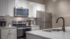Una cocina moderna con gabinetes blancos, electrodomésticos de acero inoxidable, microondas integrado, refrigerador y un lavamanos con grifo negro.