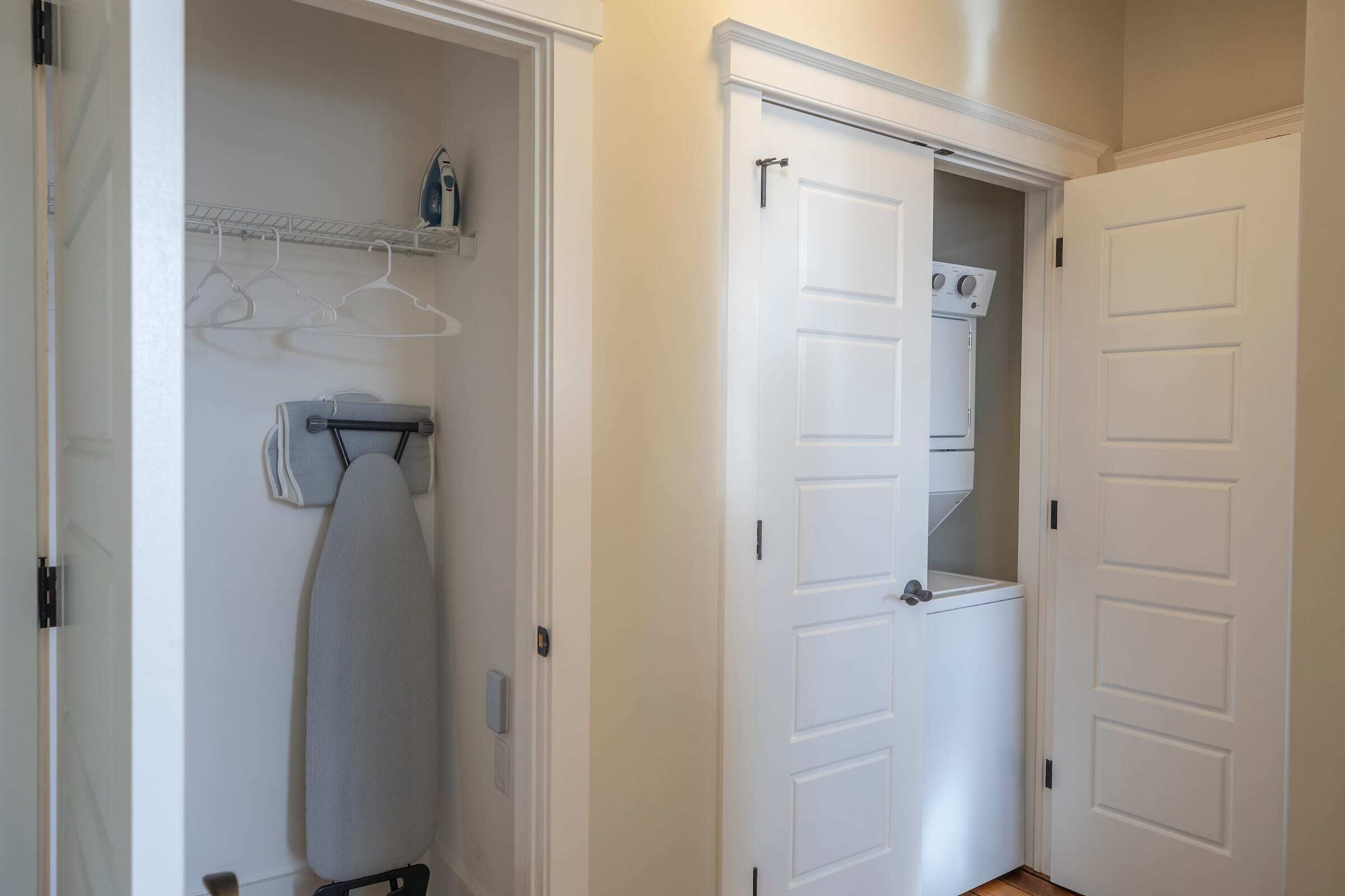 A laundry room with a dryer, ironing board, and hanging clothes rack.
