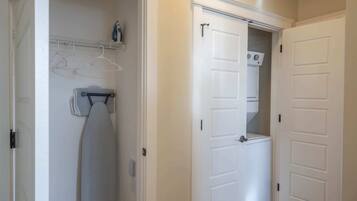 A laundry room with a dryer, ironing board, and hanging clothes rack.