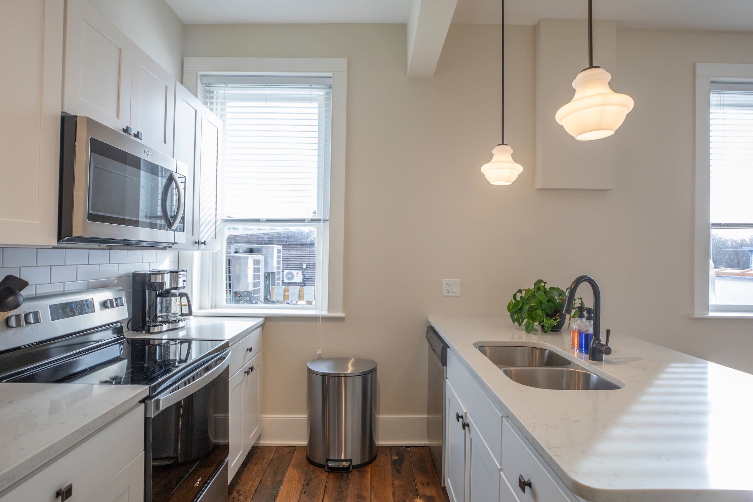 A modern kitchen with stainless steel appliances, a built-in oven, a microwave, a coffee maker, and a sink. There are two pendant lights hanging above the counter.