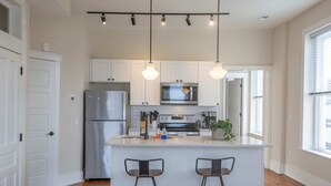 Une cuisine moderne avec des armoires blanches, des appareils en acier inoxydable et des luminaires suspendus.