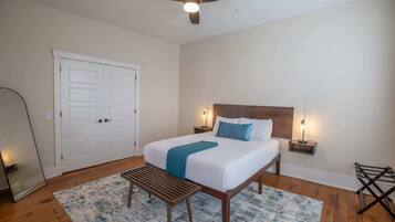 Une chambre à coucher avec un lit, des lampes de chevet, un ventilateur de plafond, un banc, une porte et un miroir.