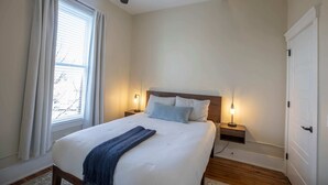 Een slaapkamer met een bed, twee nachtkastjes, een plafondventilator, een raam met gordijnen en een deur.