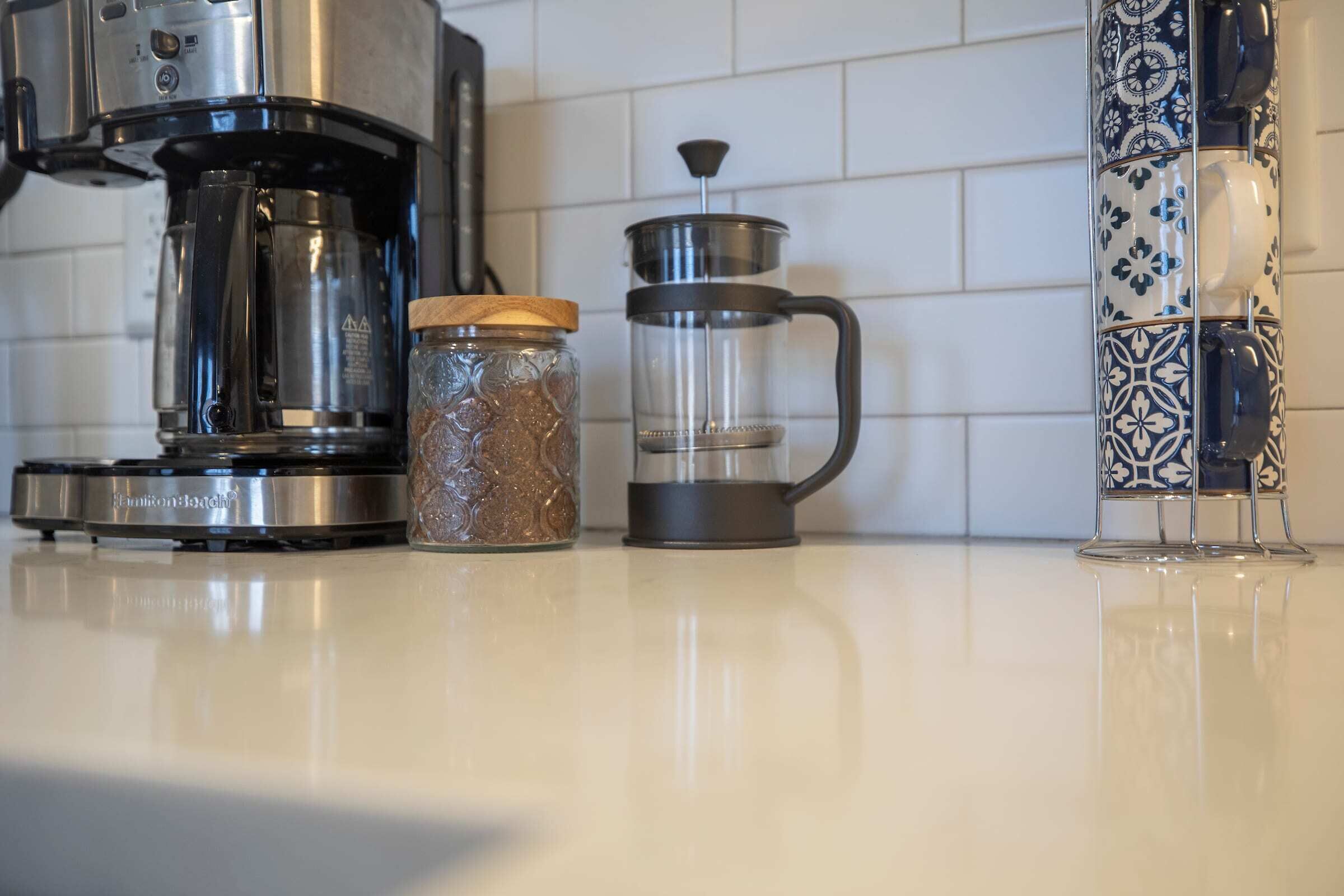 Un plan de travail de cuisine avec une machine à café, une cafetière à piston et un récipient décoratif.