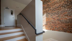 Eine Treppe mit hölzernen Stufen und einem schwarzen Geländer, die zu einem Raum mit Backsteinwand und weißer Tür führt.
