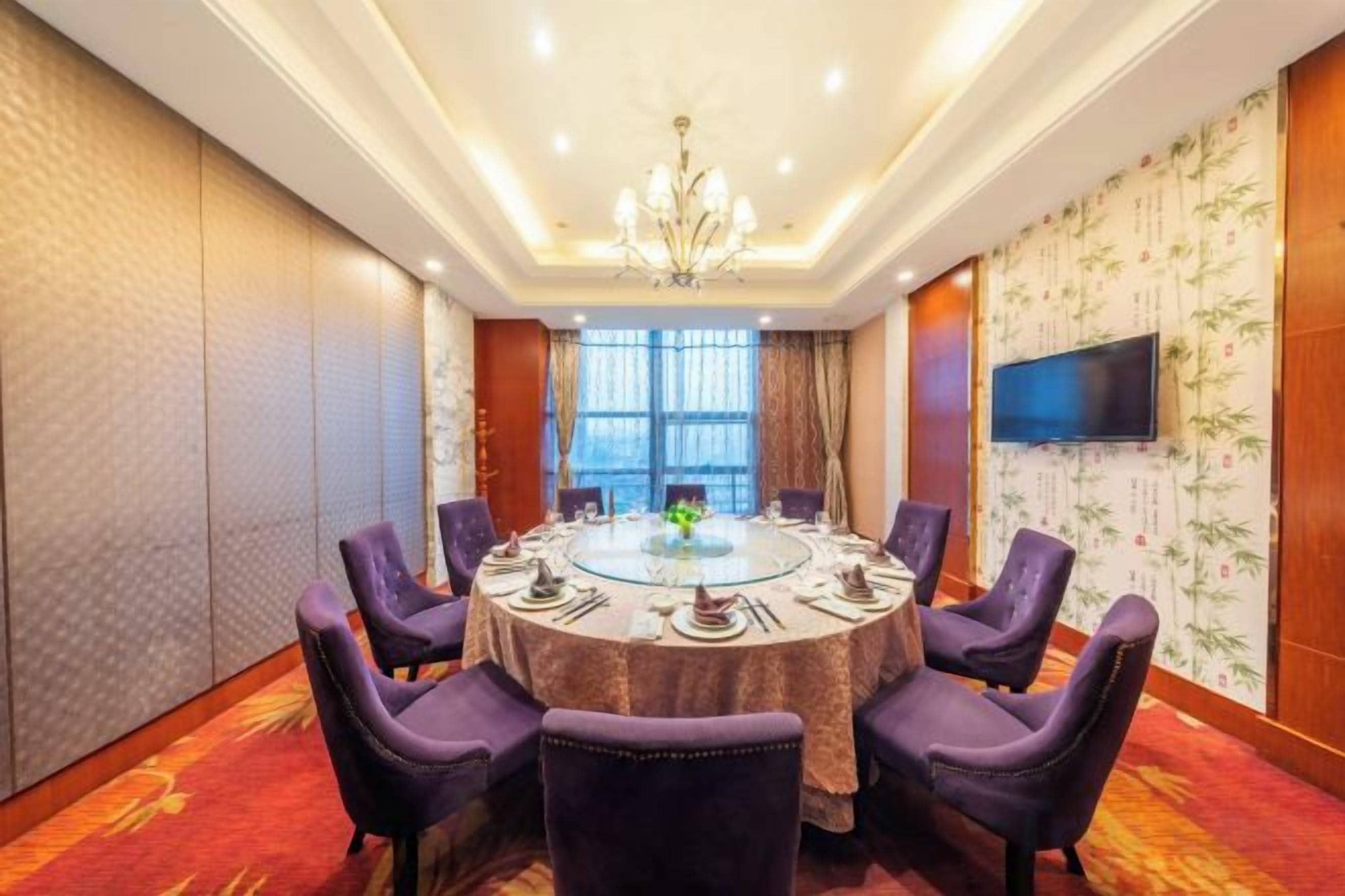A conference room with a round table, purple chairs, a chandelier, and a television on the wall.
