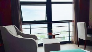Ein Hotelzimmer mit großem Fenster, einem Bett, einem Sessel und einem kleinen Tisch.