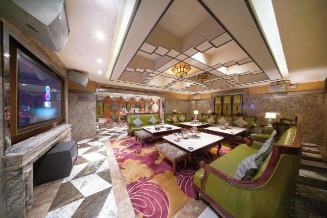 A hotel lobby with a television, seating areas, a patterned carpet, and a chandelier.