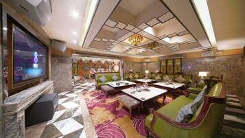 A hotel lobby with a television, seating areas, a patterned carpet, and a chandelier.