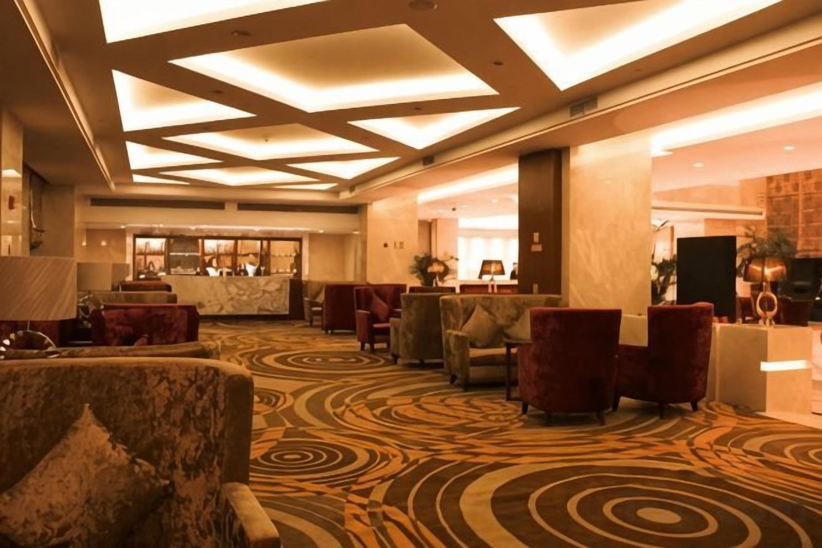 A hotel lobby with a patterned carpet, seating area, and a reception desk.