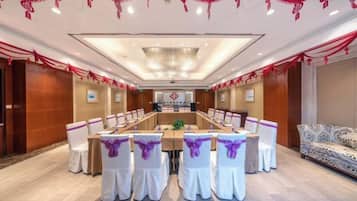 Un salón de conferencias con una larga mesa, sillas blancas con cintas moradas y cortinas rojas en el techo.