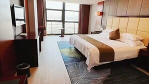 Ein Hotelzimmer mit einem großen Bett, einem Fernseher, einem Schreibtisch und Meerblick.