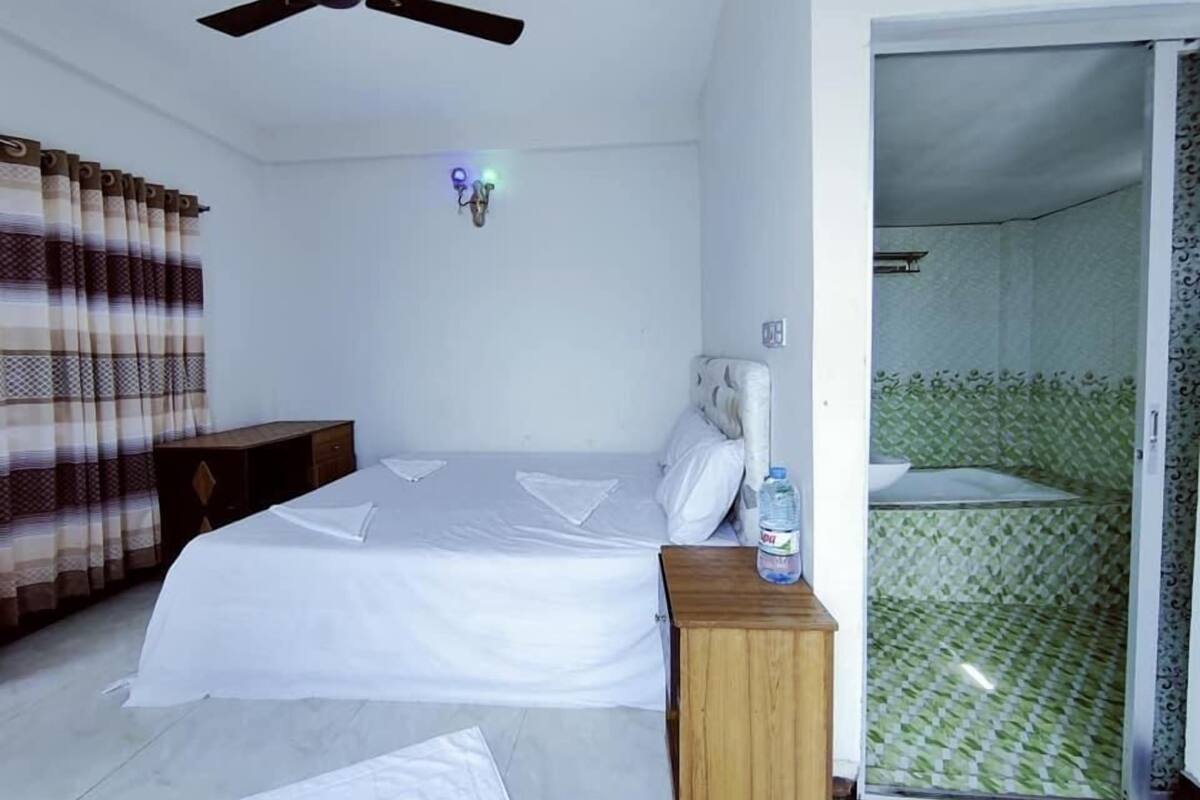 A hotel room with a bed, a wooden nightstand, a ceiling fan, and a bathroom with patterned tiles.