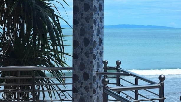 A coastal view with a metal railing, a palm tree, and a clear sky. - Hotel Royal Beach & Restaurant (Saint Martin's Island)