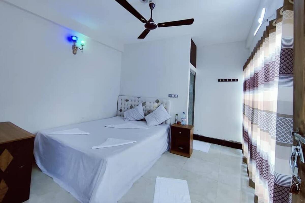 A bedroom with a bed, a nightstand, a ceiling fan, and a wall-mounted light fixture.