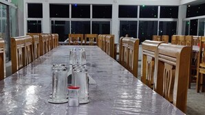A conference room with a long table, wooden chairs, and large windows. - Hotel Royal Beach & Restaurant (Saint Martin's Island)