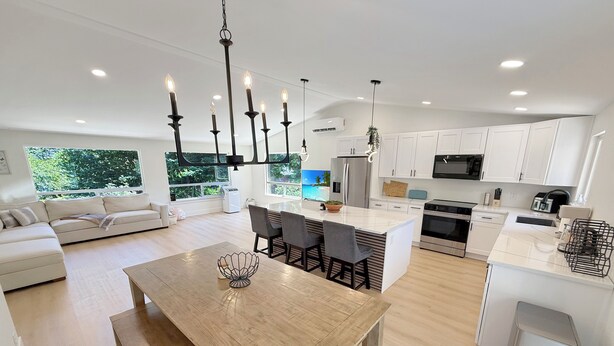 A modern kitchen with white cabinets, a central island, and a dining area with a wooden table. - Spacious 4BR Upper Duplex Unit • AC • WiFi • Quiet Area • Near SeaTac Airport (SeaTac)
