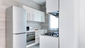 A modern kitchen with white cabinetry, a stainless steel refrigerator, an oven, and a gas stove. - Four-room apartment Scola 01 (Gabicce Mare)