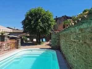 Une piscine avec un mur en pierre et un arbre en arrière-plan.