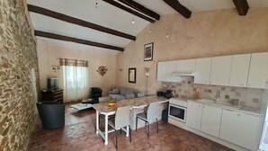 Una sala de estar acogedora con chimenea, un comedor con mesa y sillas, y una cocina con armarios blancos y salpicadero de azulejos.