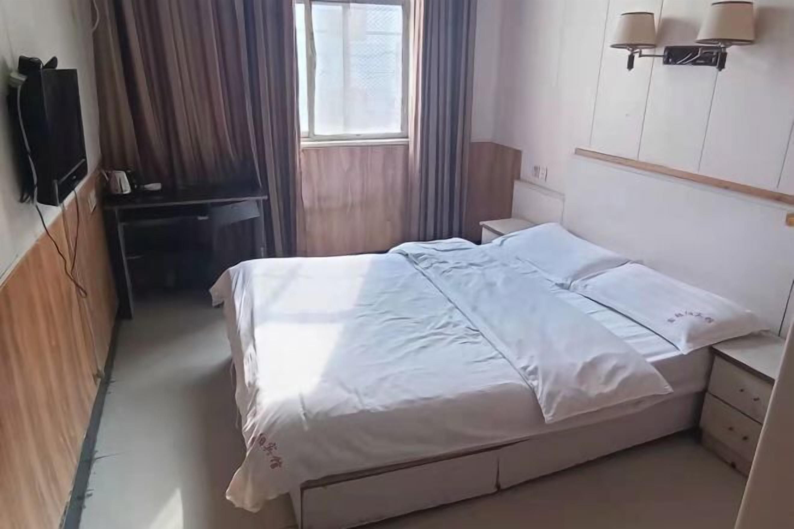 A hotel room with a bed, bedside table, lamp, TV, and curtains.