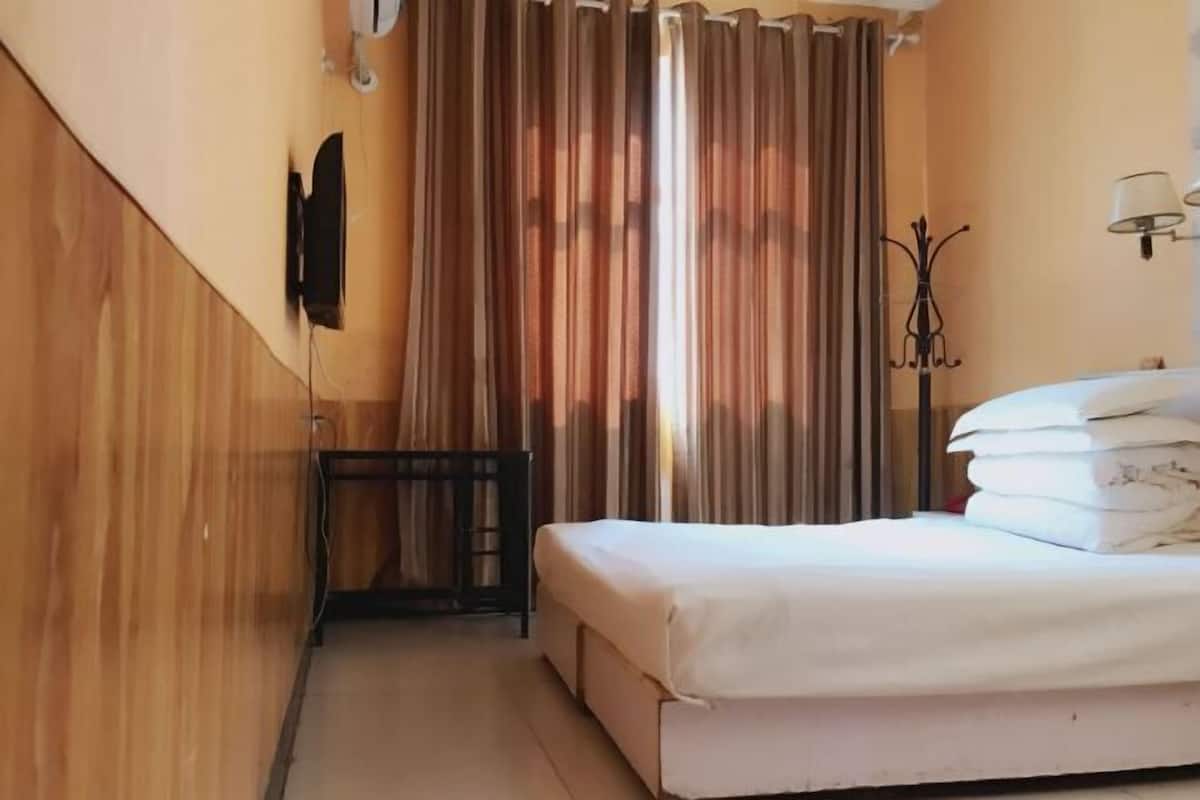 A hotel room with a bed, a television mounted on the wall, a small table, and a lamp.